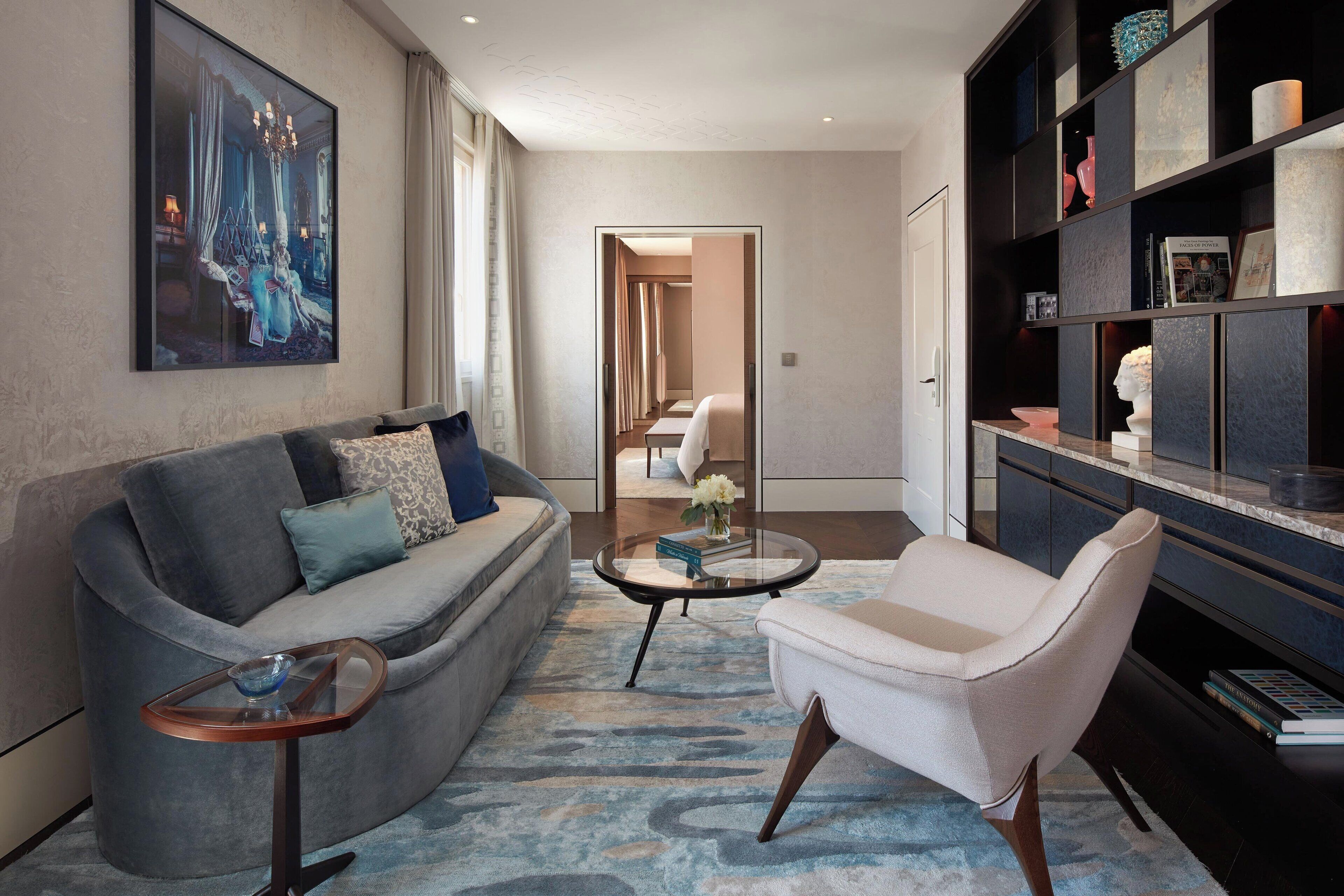 A modern living room with a grey sofa, a white armchair, a glass coffee table, and a bookshelf.