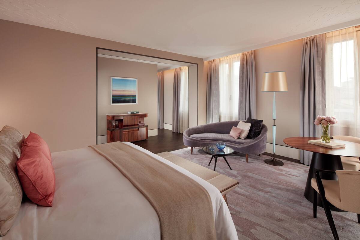A hotel room with a large bed, a sofa, a small table, and a chair.