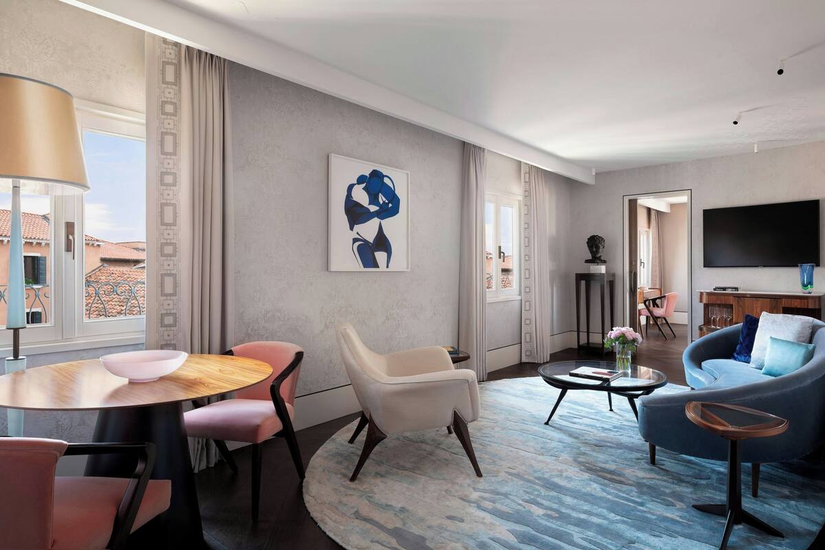 A modern living room with a round wooden table, a beige armchair, a blue sofa, and a flat-screen TV mounted on the wall.