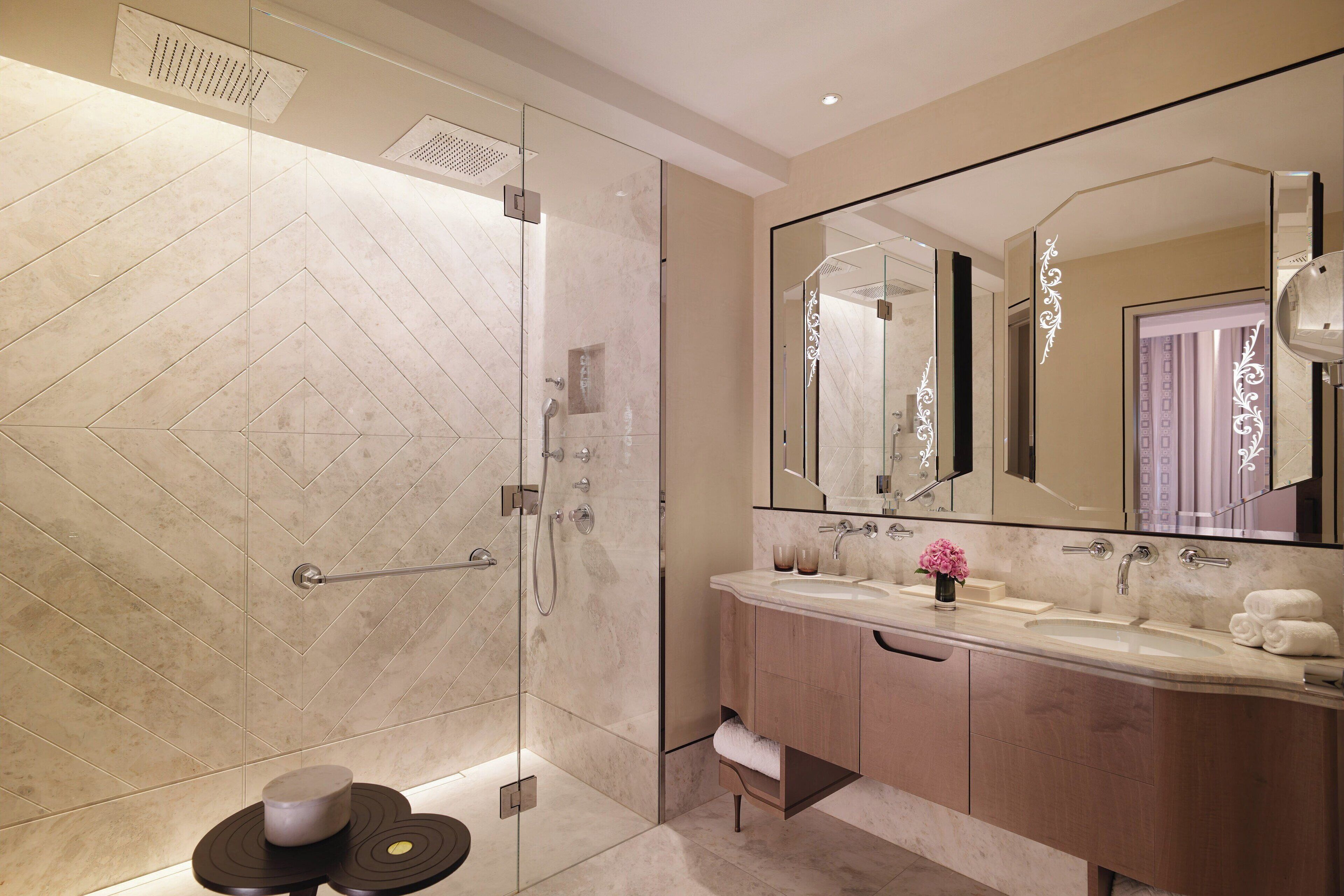 Un baño moderno con ducha envuelta en vidrio, tocador con un espejo grande y suelo de mármol.