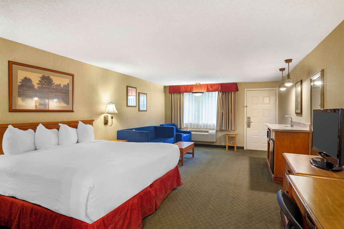A hotel room with a large bed, a desk, a television, a chair, and a window with curtains.