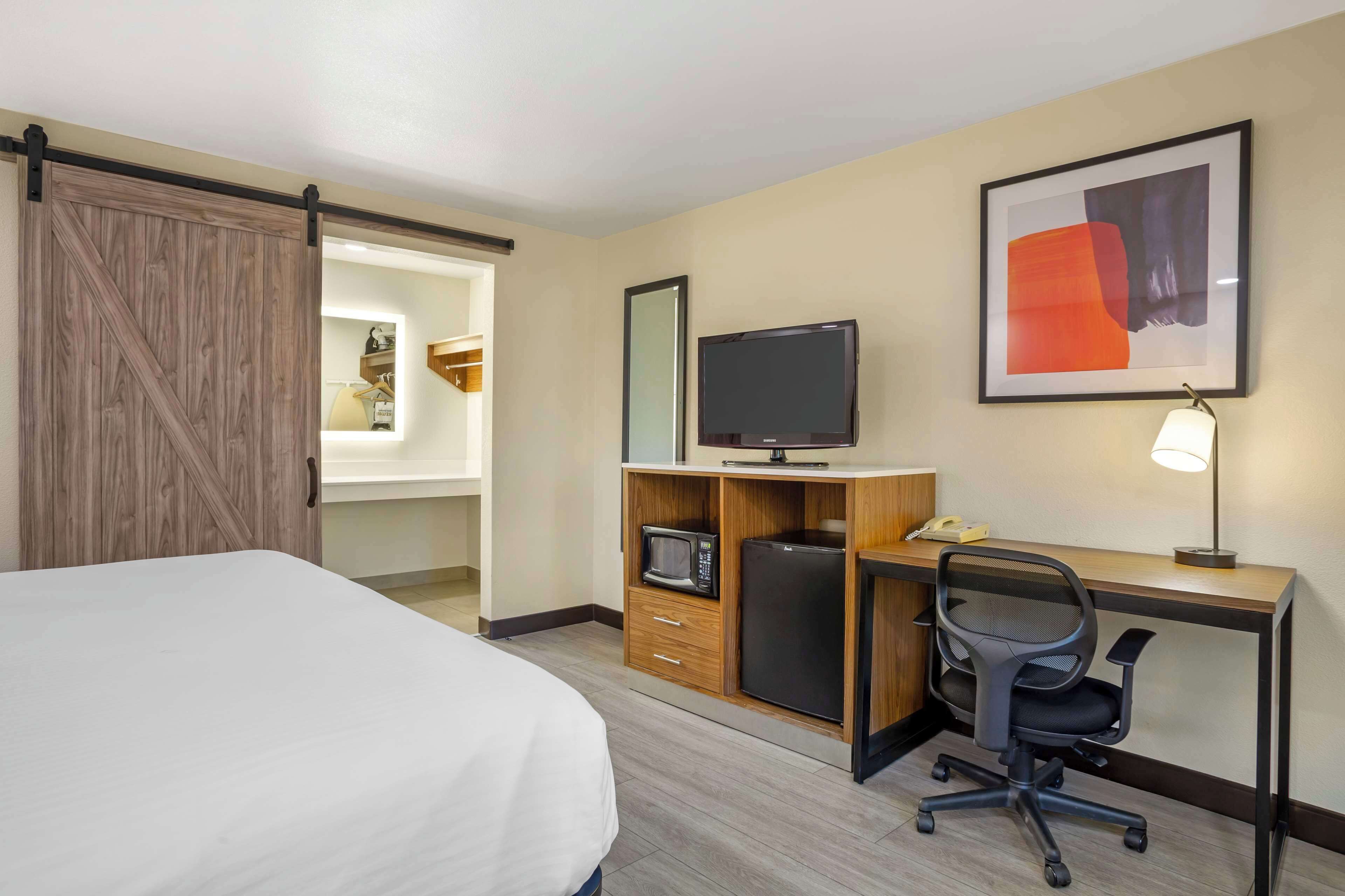 Una habitación de hotel con una cama, un escritorio con computadora, televisor y microondas.