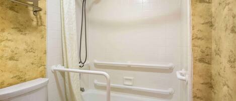 A bathroom with a toilet, a shower with grab bars, and a bathtub.