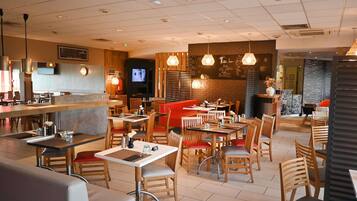 Un restaurant moderne doté d’un bar, de plusieurs types de sièges, notamment des banquettes et des tables, et d’un écran de télévision fixé au mur.