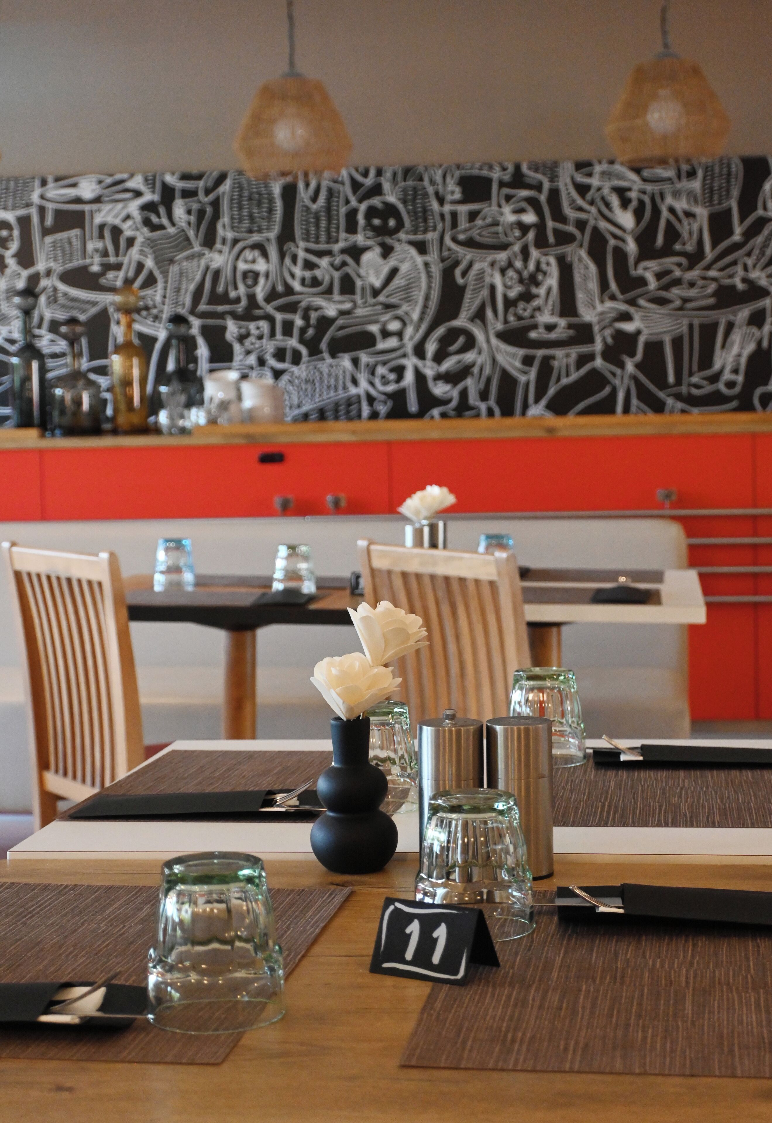 A dining table set with numbered place settings, a vase with flowers, and a black and white abstract mural in the background.