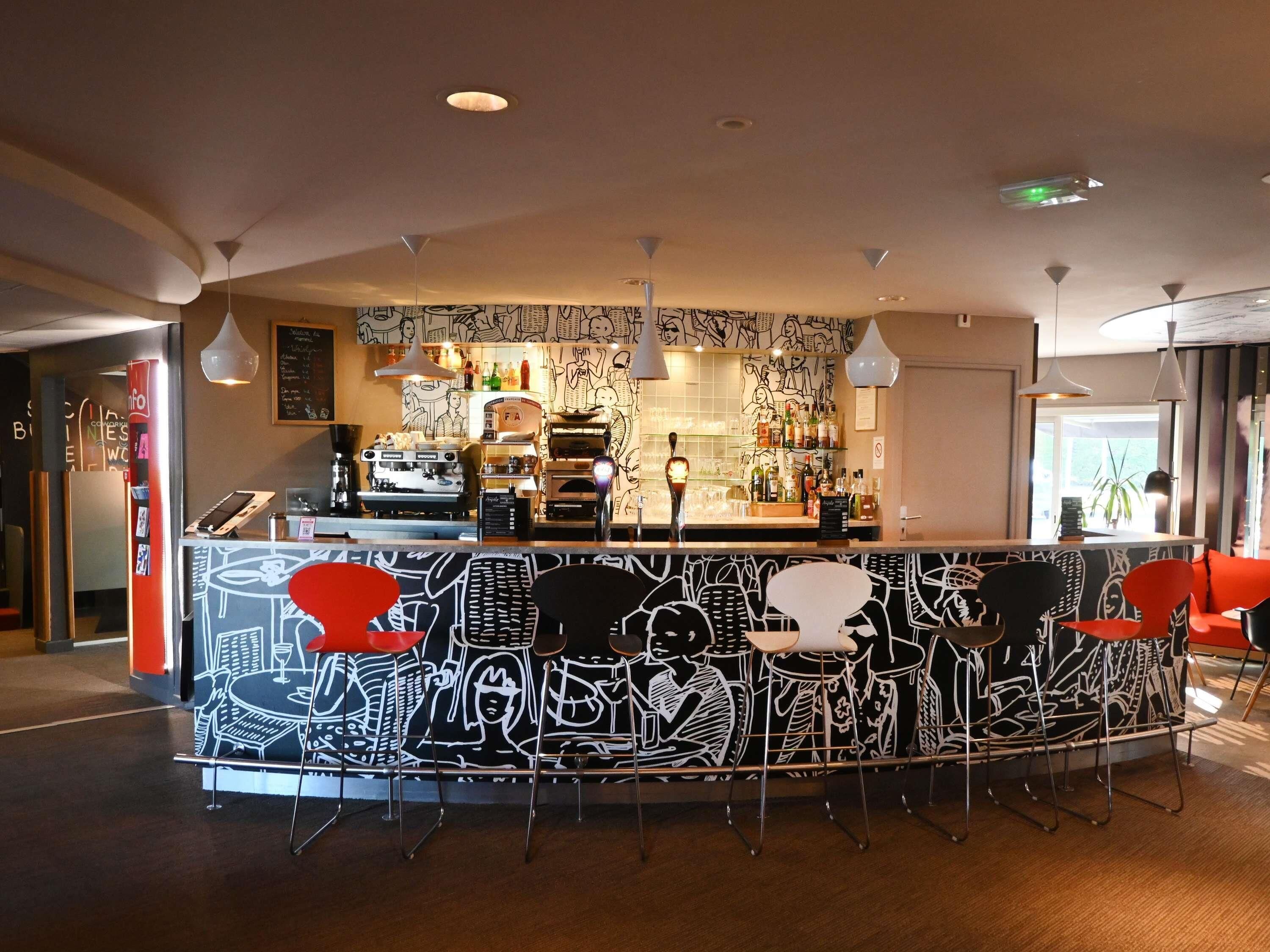 Un espace bar comprenant un comptoir, des tabourets de bar et une fresque murale représentant des figures abstraites.
