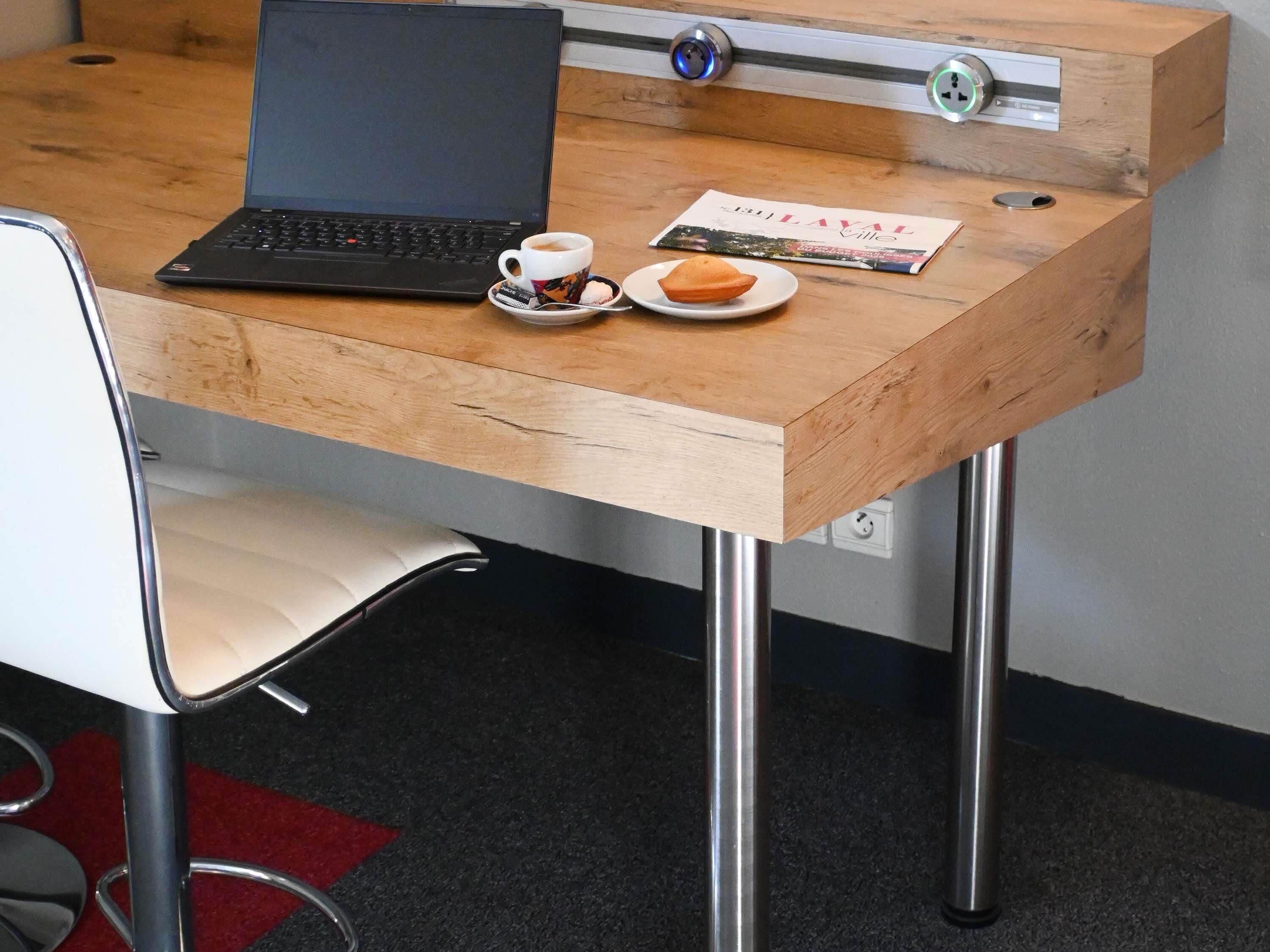A wooden desk with a laptop, a cup of coffee, and a plate with a pastry.
