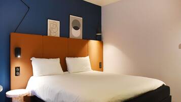 Una habitación de hotel con una cama, una mesita de noche, una lámpara de pared y dos obras de arte enmarcadas.