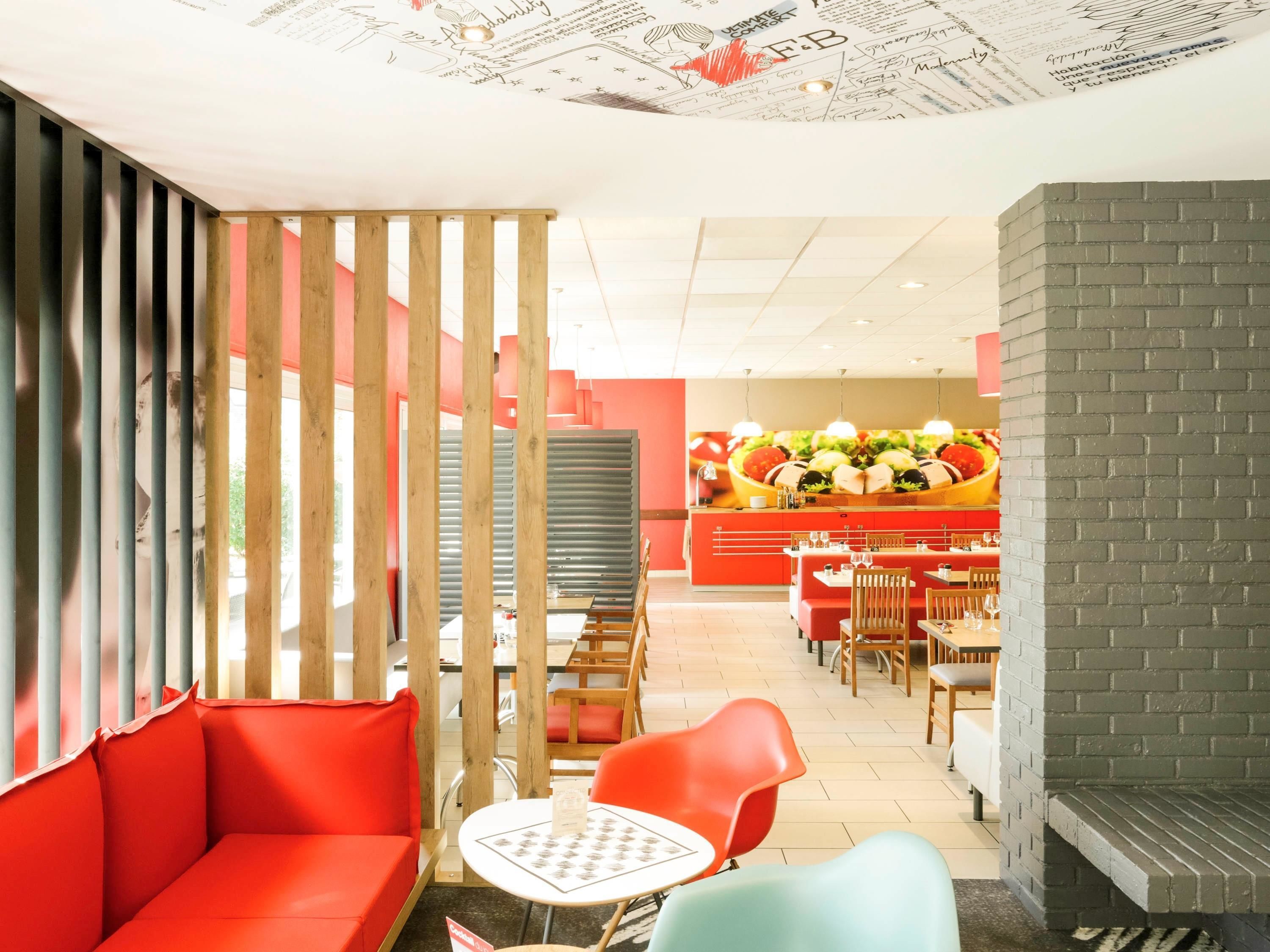 Ein Restaurantinneres mit roter und grauer Gestaltung, Holzvertäfelungen und einer zentralen Theke mit Lebensmitteln.