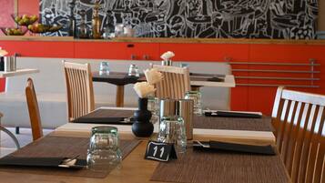 Interior de restaurante con pared de diseño en blanco y negro, sillas de madera, una mesa con tarjeta de número y lámparas colgantes.