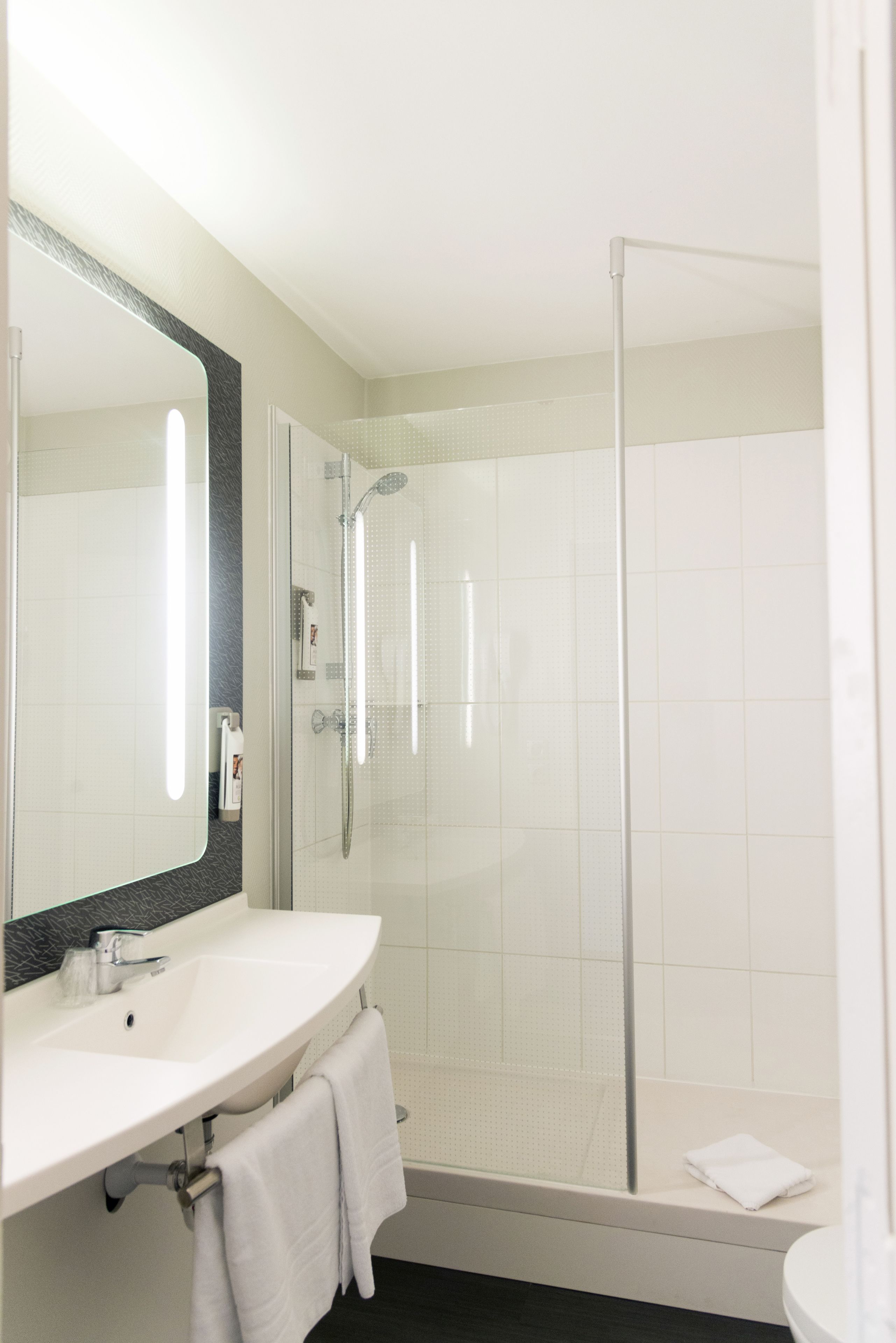 Un baño moderno con un lavabo blanco, un espejo grande y una ducha con cerramiento de vidrio.