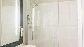 Un baño moderno con un lavabo blanco, un espejo grande y una ducha con cerramiento de vidrio.