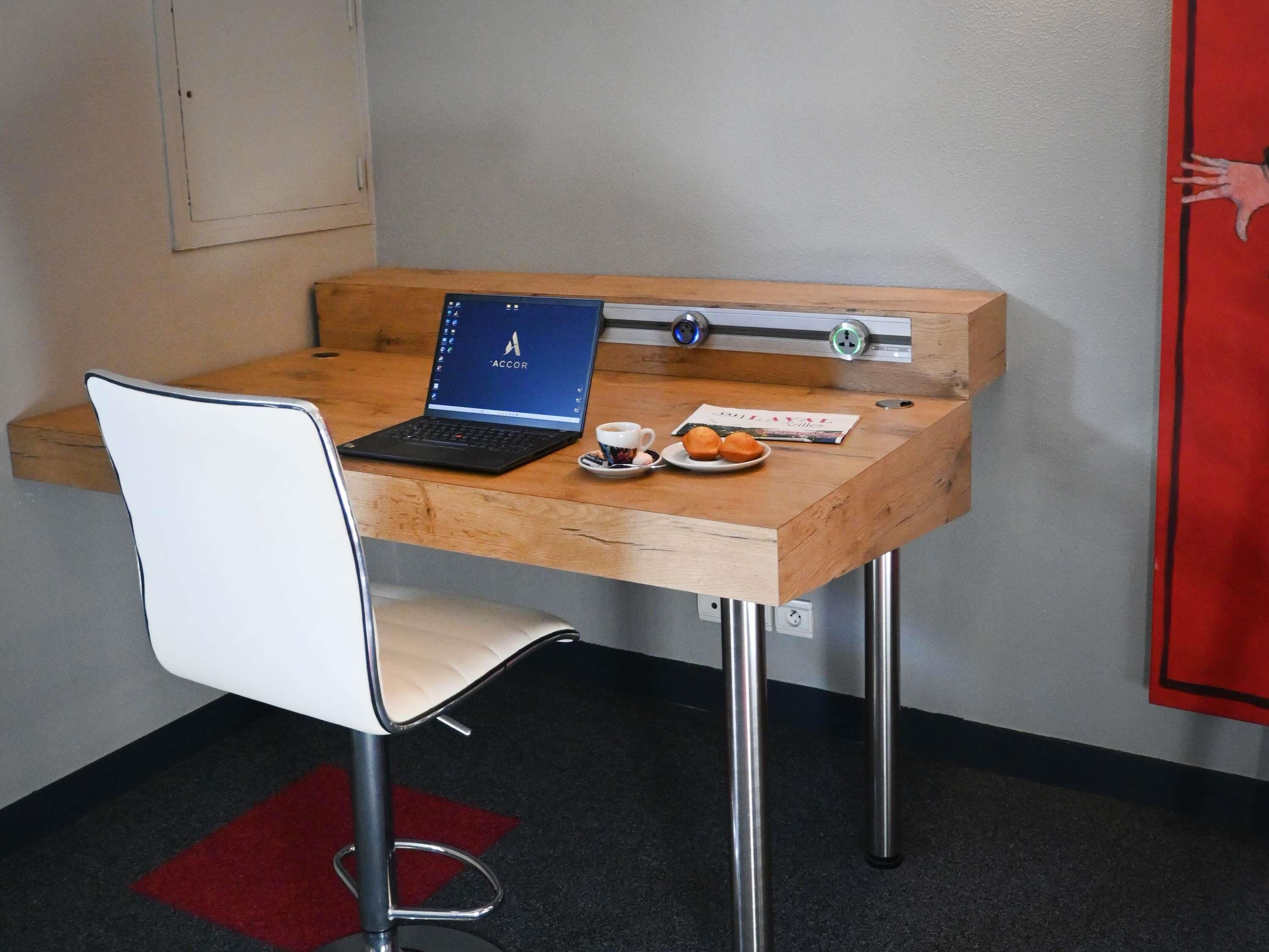 A small wooden desk with a laptop, a cup of coffee, and a plate of pastries.