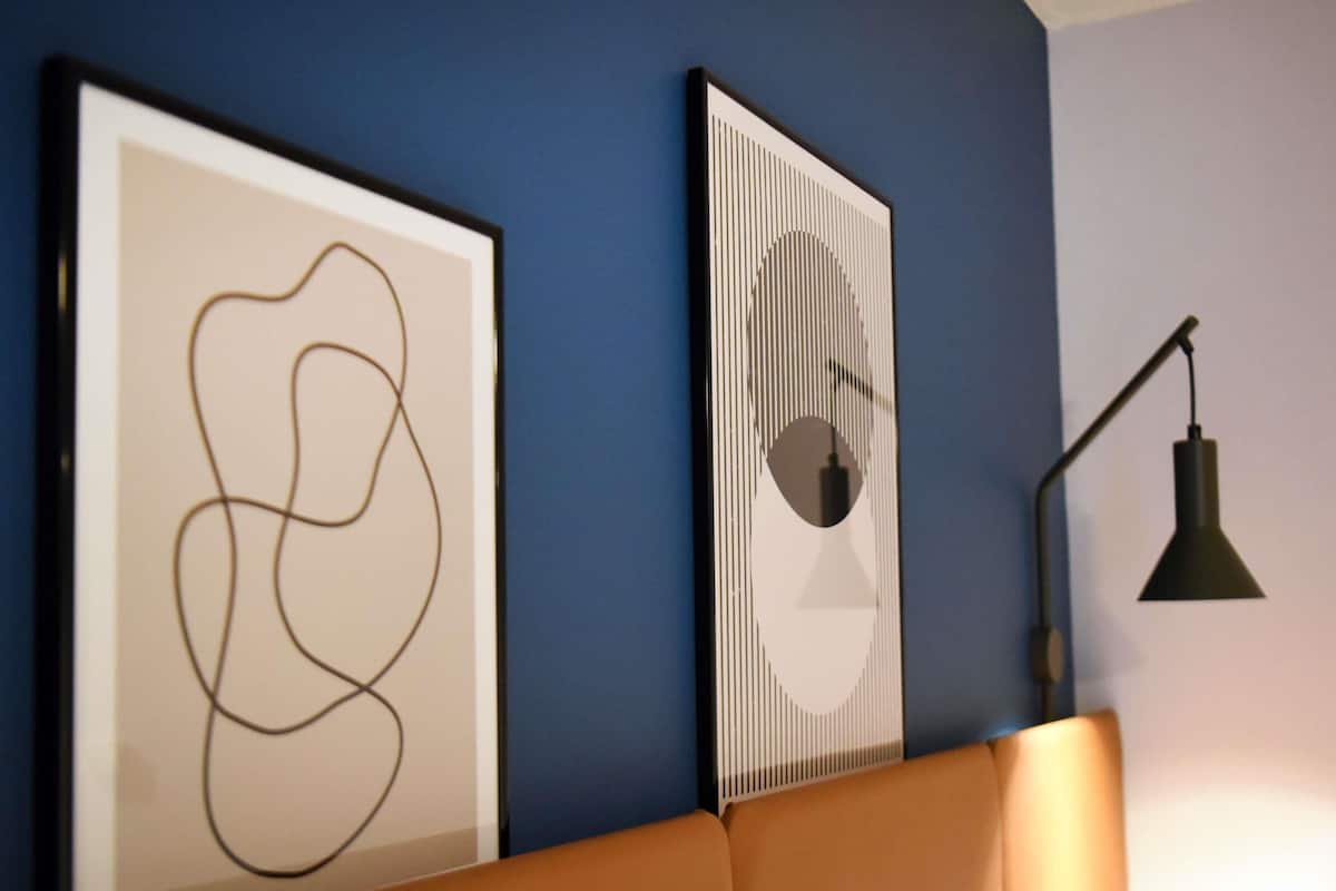 Quarto com parede azul, uma obra de arte abstrata emoldurada, luminária moderna e sofá marrom.