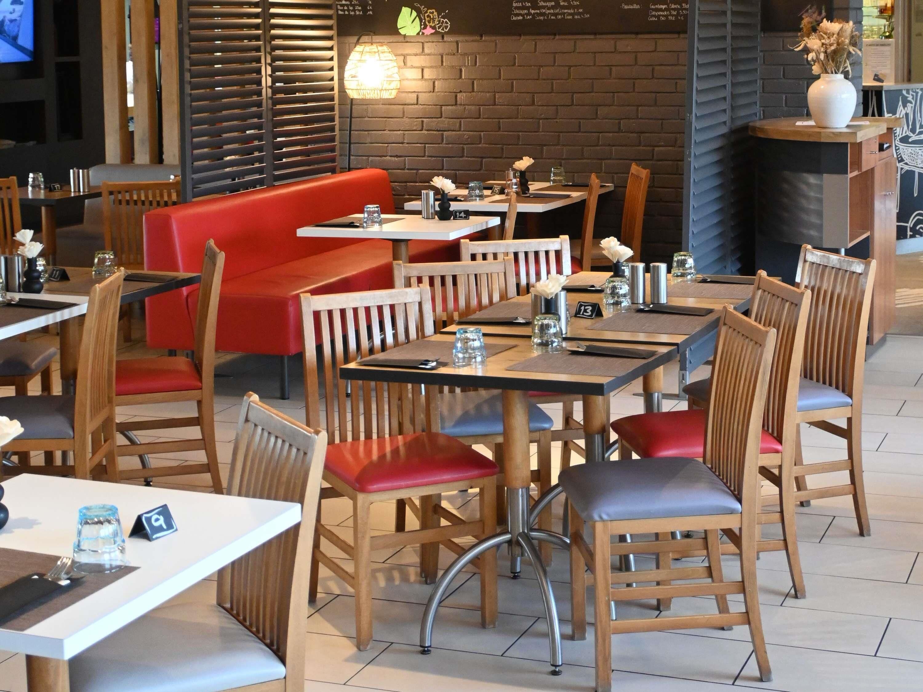 Un interior de restaurante con mesas y sillas de madera, cabinas tapizadas en rojo y una pared de ladrillo.