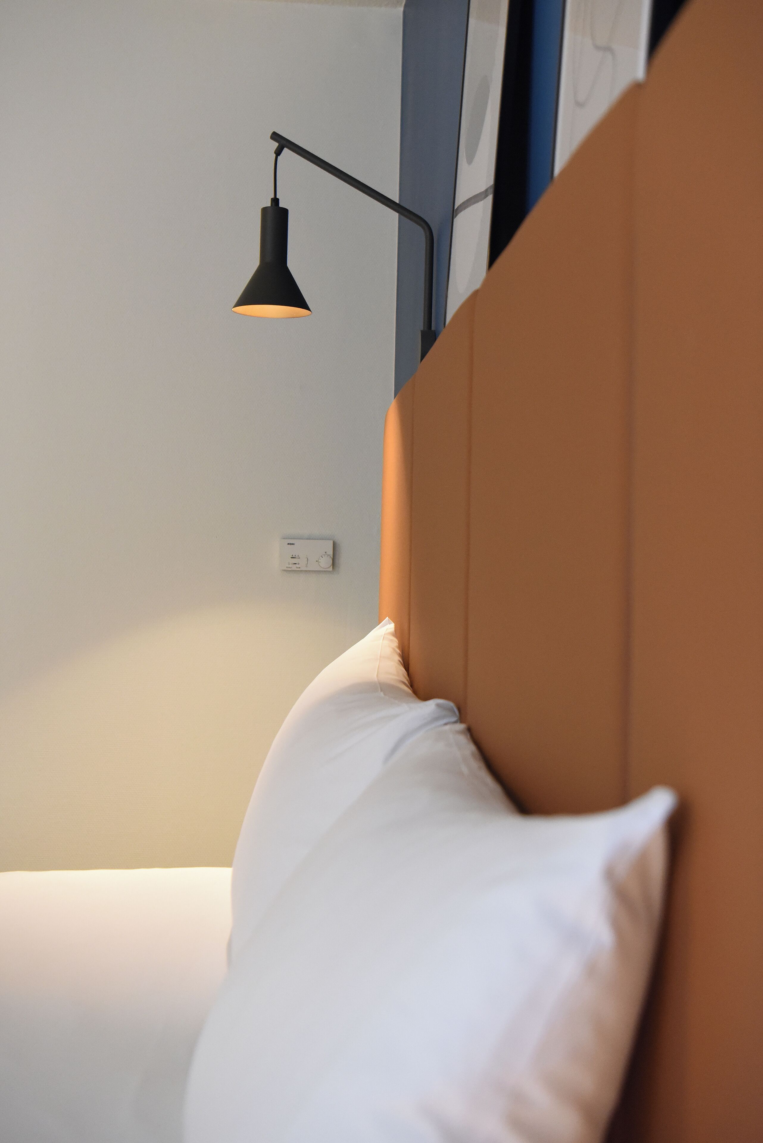 Ein Schlafzimmer mit Bett, Nachttisch, Wandlampe und Thermostat.