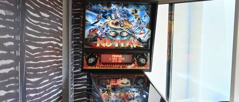 A pinball machine in a room with patterned walls and a large window.
