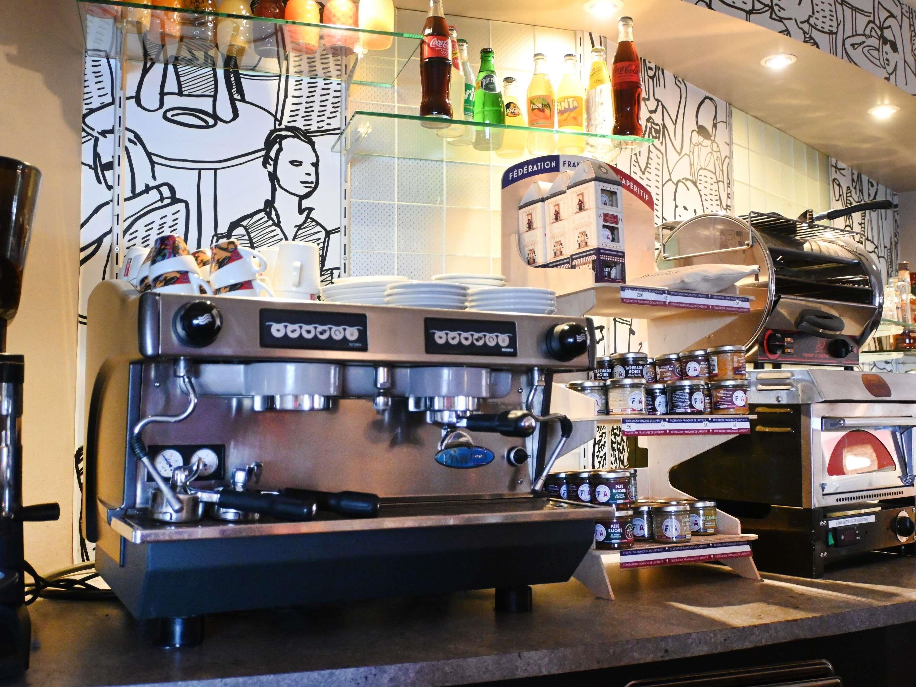 Une machine à café dotée d’un mousseur à lait, d’un moulin à café et d’un présentoir où sont exposés des grains de café et des pots d’assaisonnements.