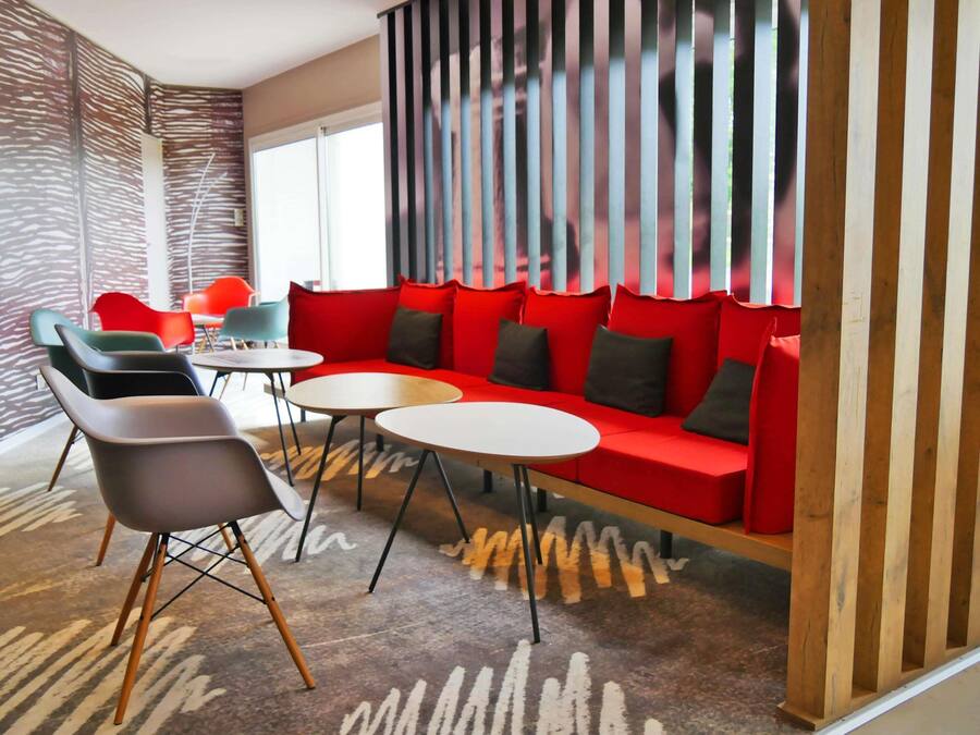 A modern lounge area with a red sofa, black and green chairs, and a patterned carpet.