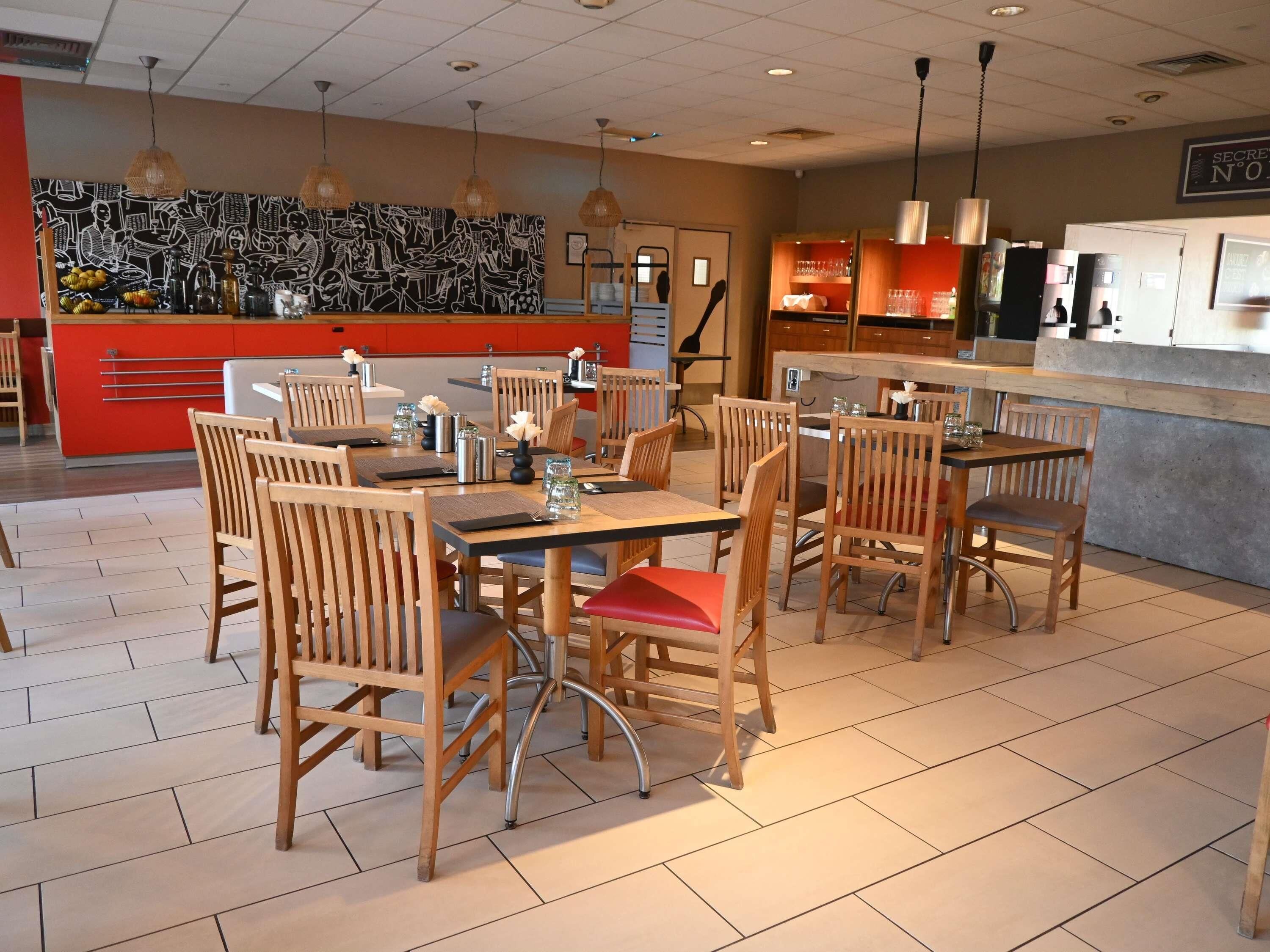 Un restaurante con mesas y sillas de madera, una barra roja y un mural blanco y negro en la pared.