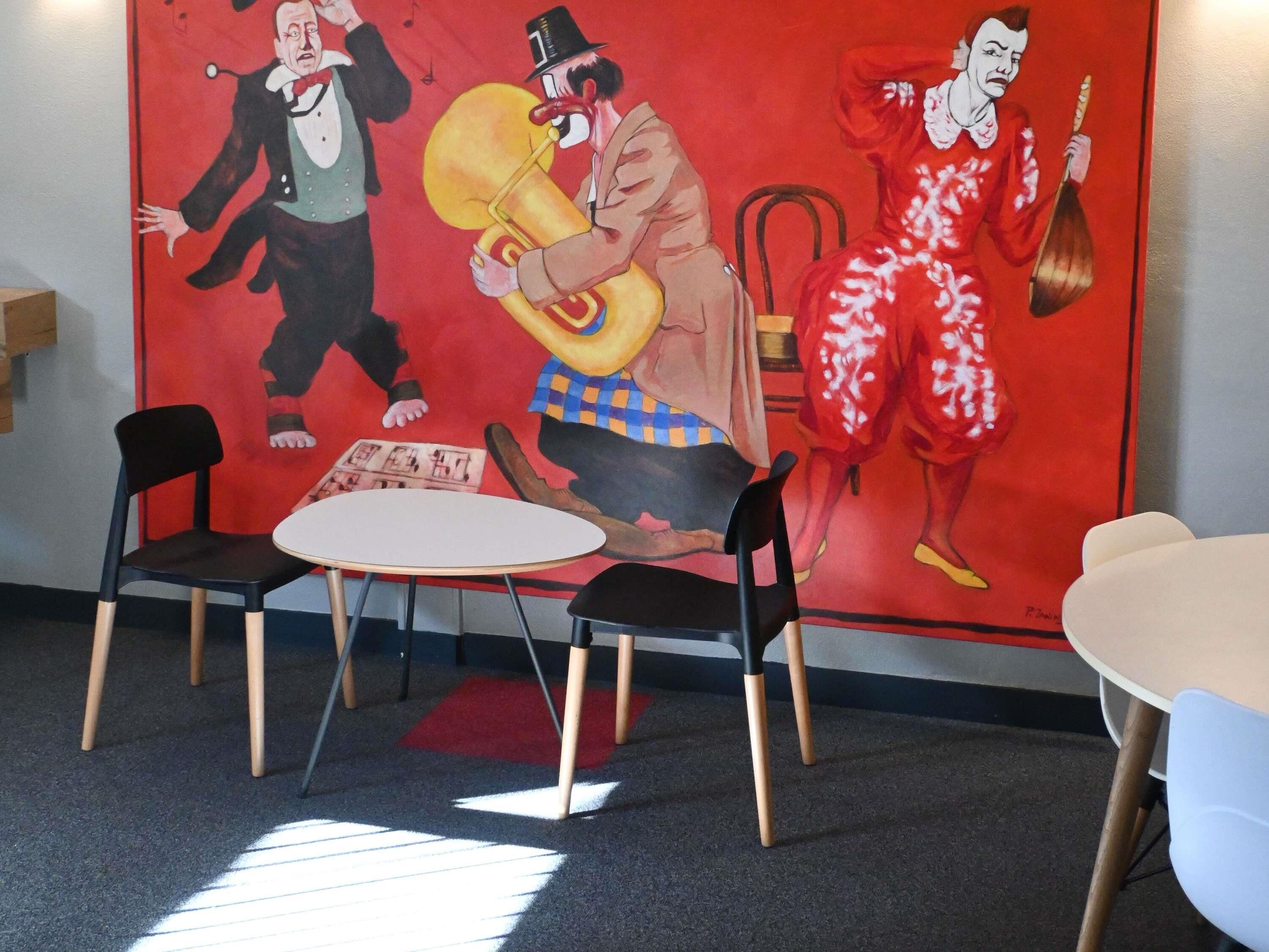Una habitación con un mural rojo, dos sillas negras, una mesa blanca y una alfombra roja.