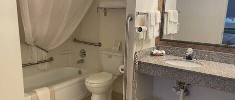 A bathroom with a bathtub, toilet, vanity with a mirror, and a shower curtain.