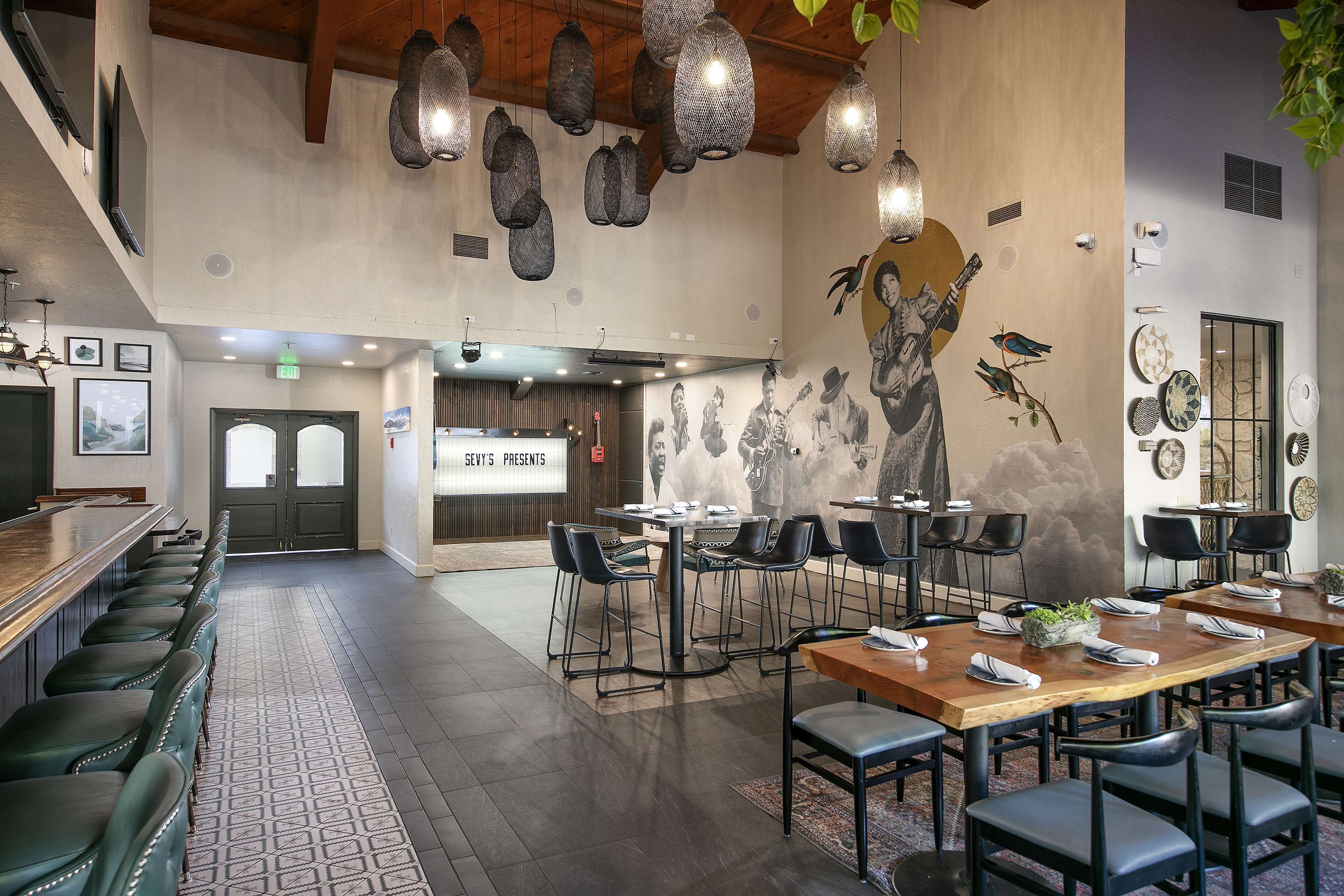 A spacious restaurant with high ceilings, hanging pendant lights, and a mural on the wall.