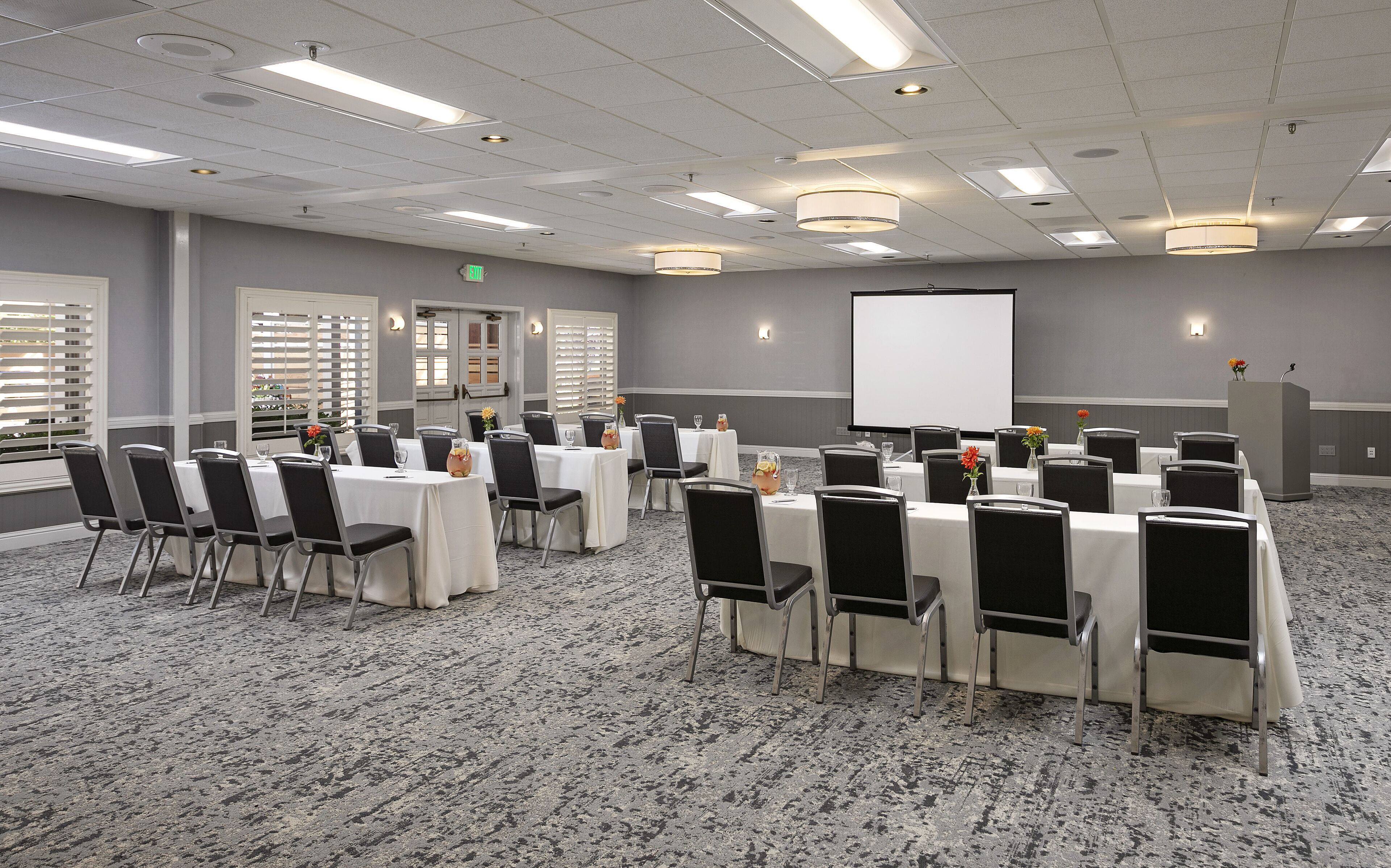 A conference room with tables, chairs, a projector screen, and a podium.