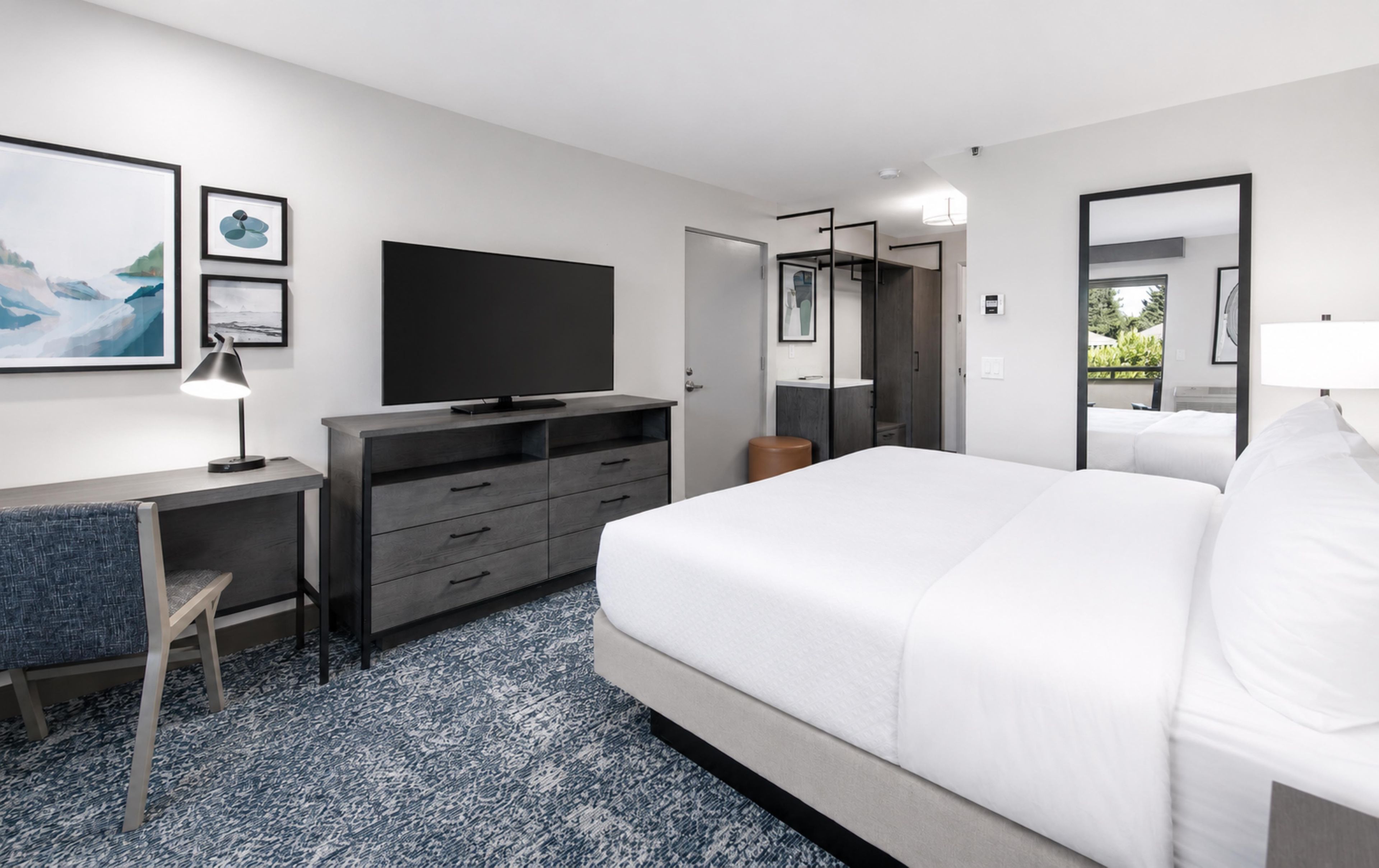 Ein Hotelzimmer mit einem Bett, einem Schreibtisch mit Computer, einem Fernseher und einem Kleiderschrank.