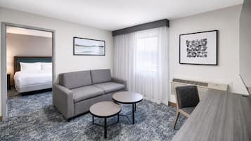 A hotel room with a bed, a grey sofa, two round tables, and two framed pictures on the walls.