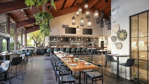 A spacious restaurant with a long wooden table, multiple chairs, hanging pendant lights, and a bar area with shelves of bottles. - Seacliff Inn Aptos, Tapestry Collection by Hilton (Aptos)