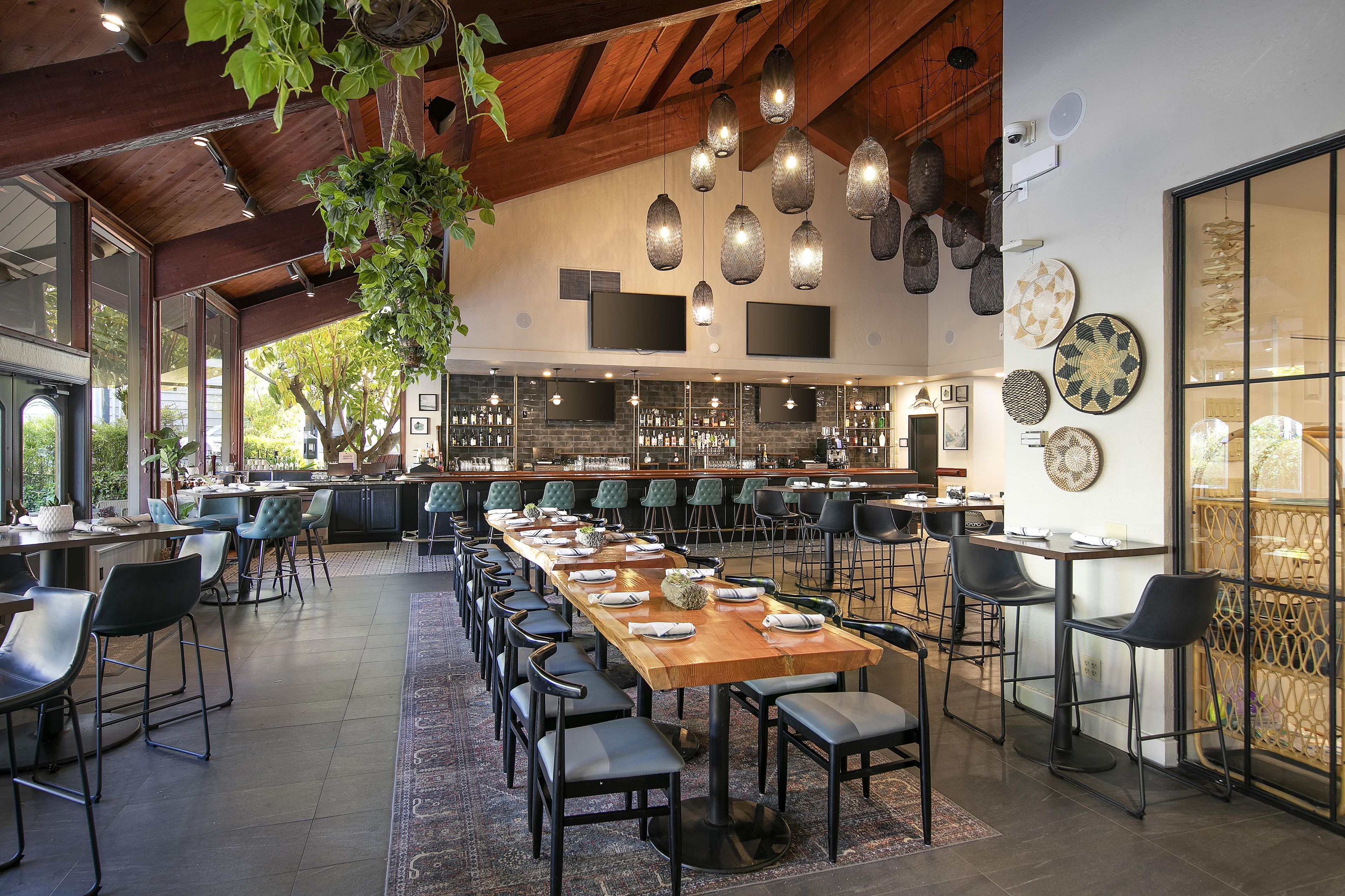 A spacious bar area with multiple seating arrangements, a long counter, and hanging pendant lights.