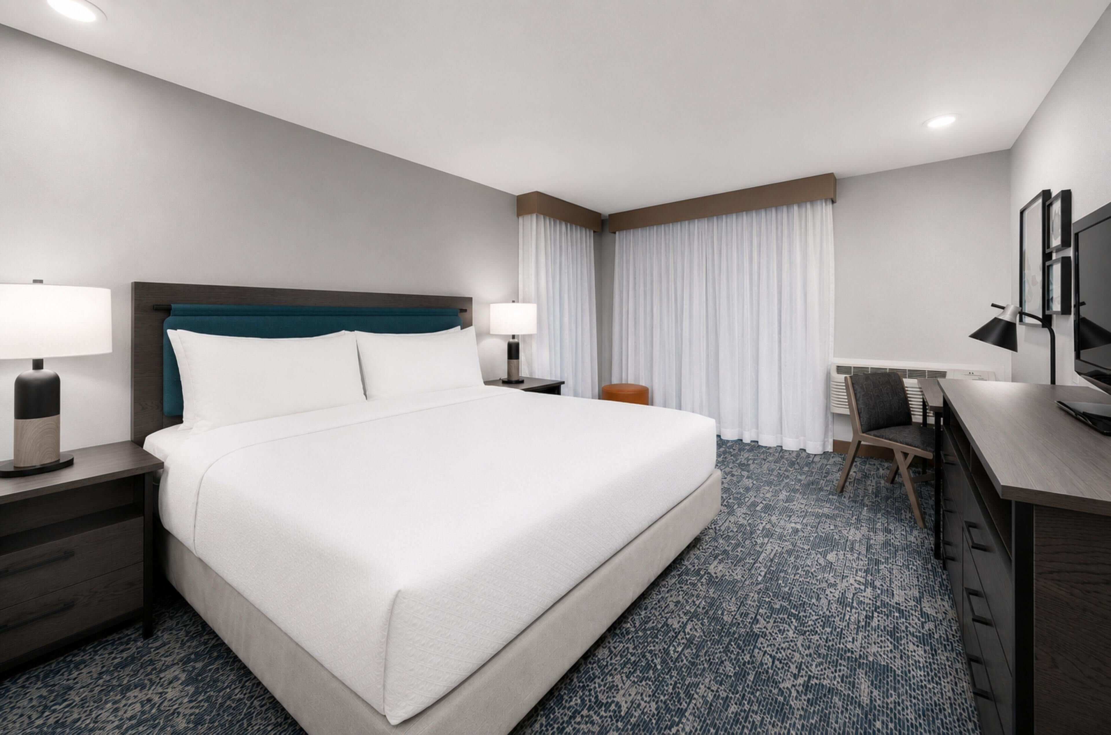 Une chambre d’hôtel avec un grand lit, des tables de chevet, un bureau, une chaise et un téléviseur.