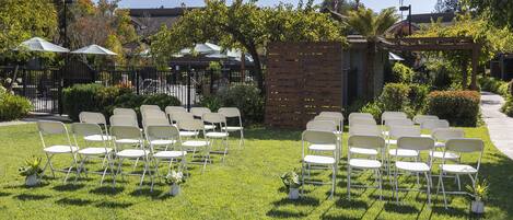 Un espacio al aire libre con césped y sillas blancas dispuestas en filas, probablemente para un evento.