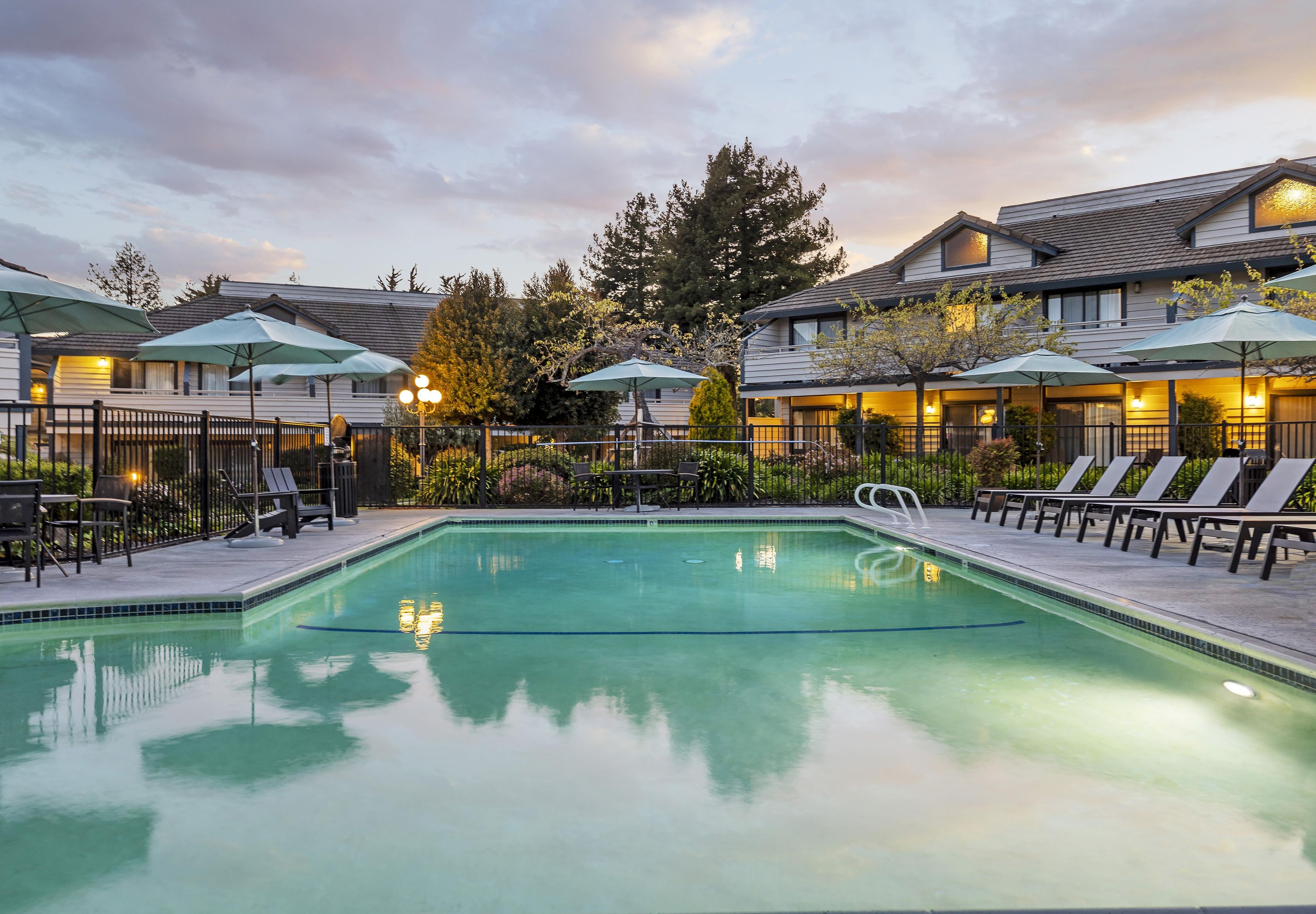 Une piscine entourée de bâtiments dotés de terrasses, avec des chaises longues et des parasols à proximité.