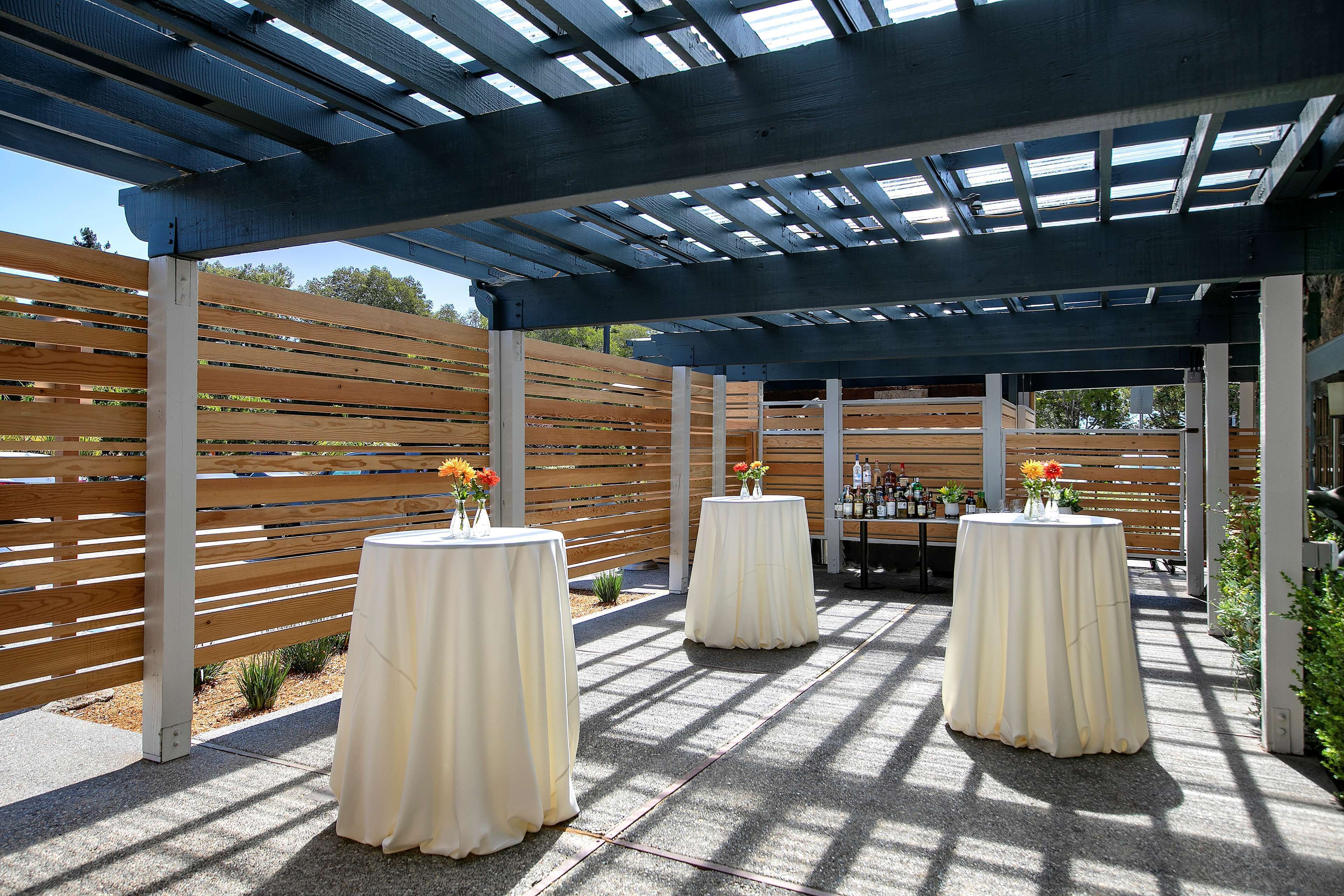 An outdoor patio area with covered seating and tables, wooden slats, and a pergola structure.