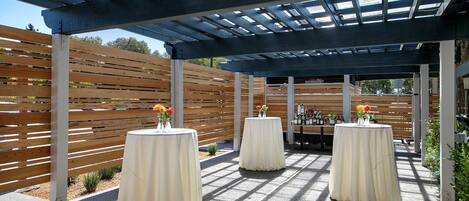 An outdoor patio area with covered seating and tables, wooden slats, and a pergola structure.