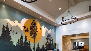 A lobby with a mural of a forest and moon, seating area with sofas and a coffee table, and a stone wall. - Seacliff Inn Aptos, Tapestry Collection by Hilton (Aptos)