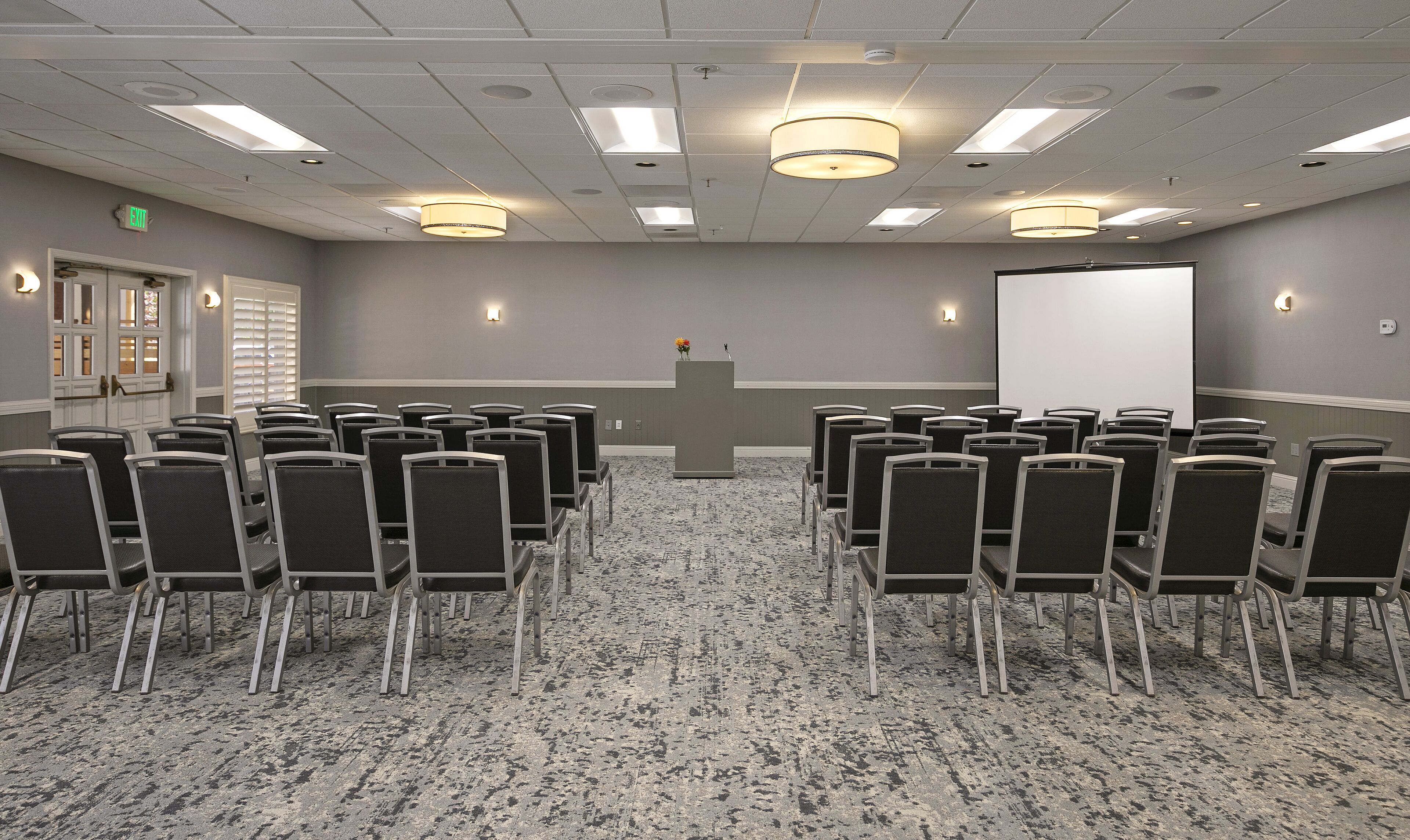 A conference room with rows of chairs, a podium, a whiteboard, and a projector screen.
