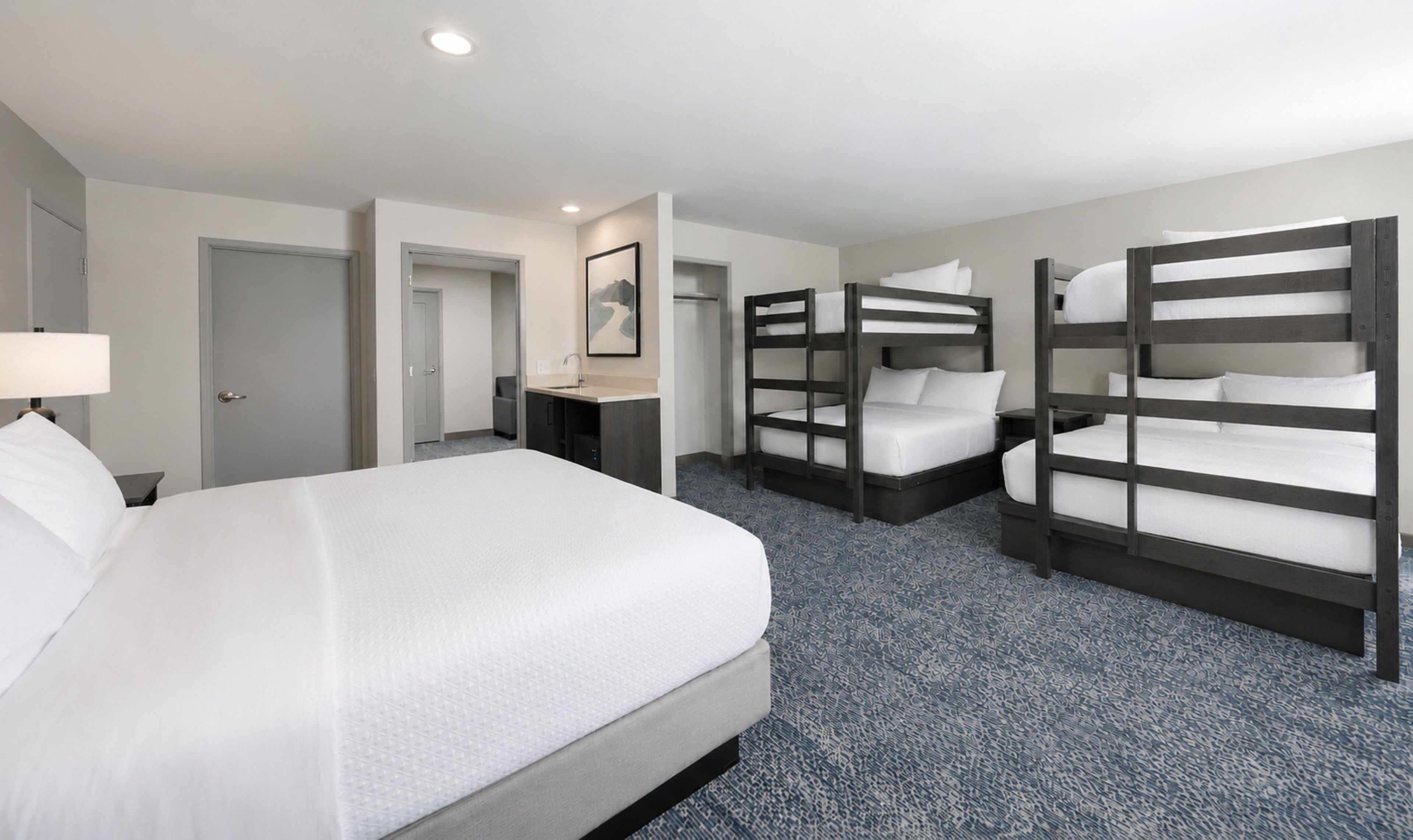 A hotel room with a large bed, two bunk beds, a desk, and a shower area.