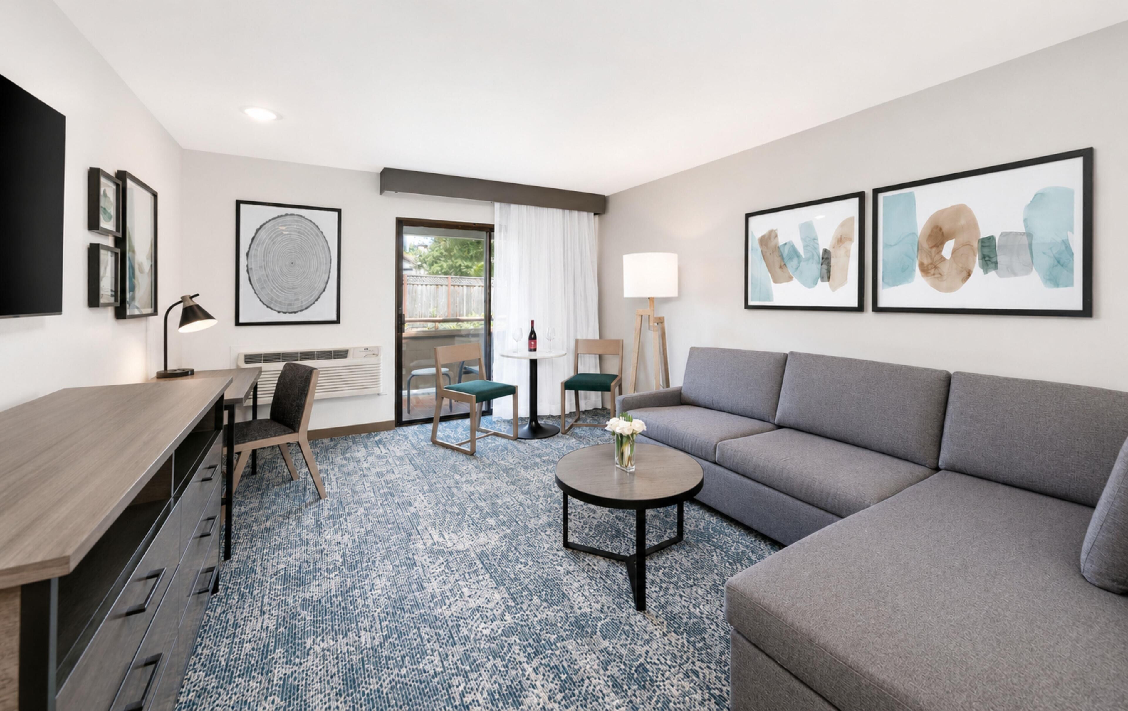 A modern hotel room with a sofa, a desk, a chair, a coffee table, and artwork on the walls.
