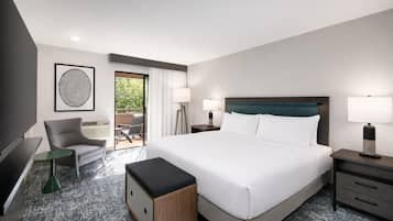 A hotel room with a large bed, a desk, a chair, a TV, and a view of the outdoors.