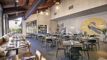 Un restaurante espacioso con techos altos, iluminación moderna y un mural de un ave en la pared.