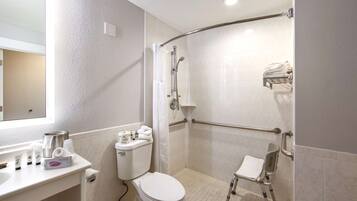 Un baño con inodoro, lavamanos con artículos de aseo, ducha con barra de apoyo y banco accesible para sillas de ruedas.