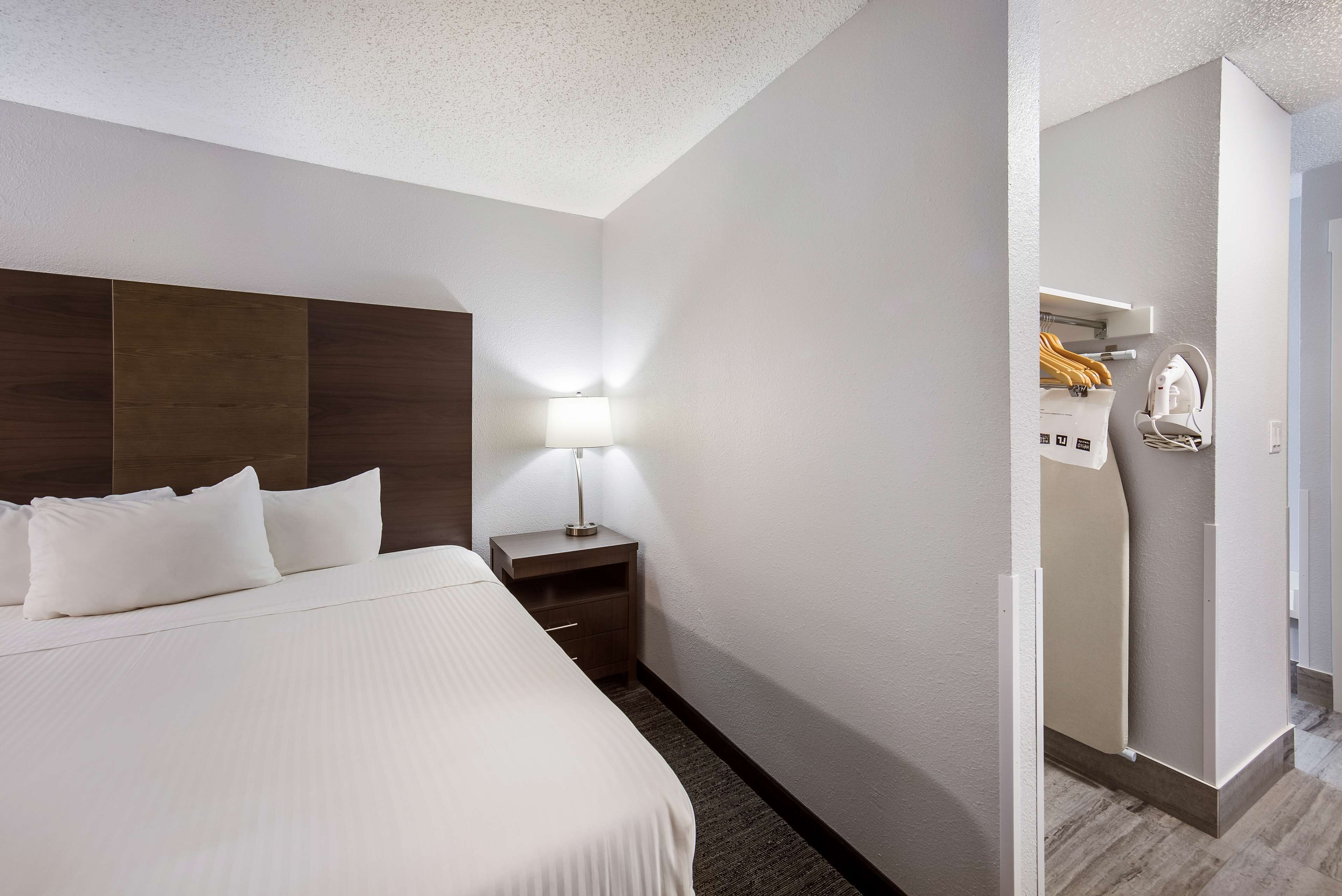 A hotel room with a large bed, a nightstand with a lamp, and a wardrobe.