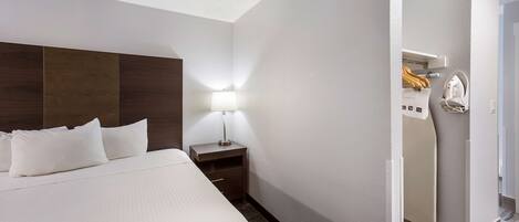 A hotel room with a large bed, a nightstand with a lamp, and a wardrobe.