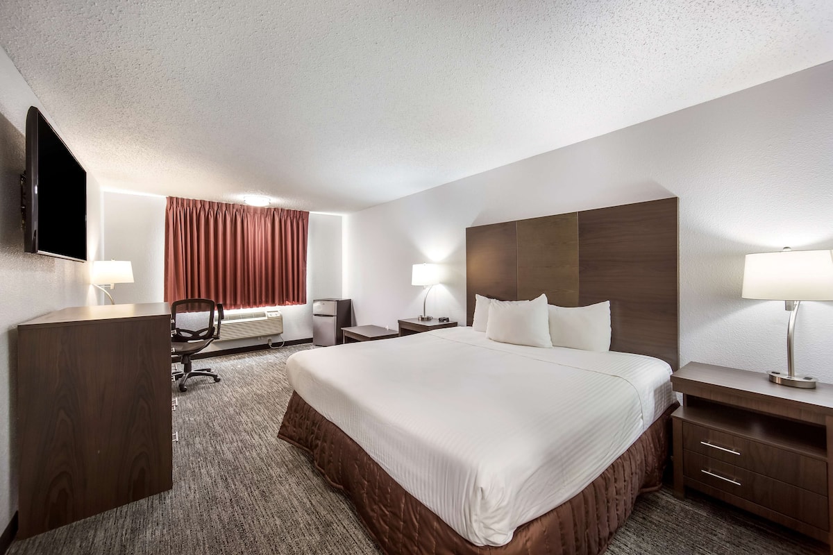 A hotel room with a large bed, a desk, a chair, a flat-screen TV, and a window with curtains.
