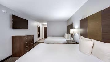 A hotel room with a large bed, a dresser, a flat-screen TV mounted on the wall, and a bedside table with a lamp.
