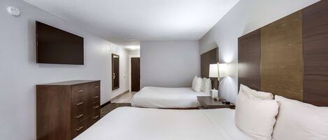 A hotel room with a large bed, a dresser, a flat-screen TV mounted on the wall, and a bedside table with a lamp.