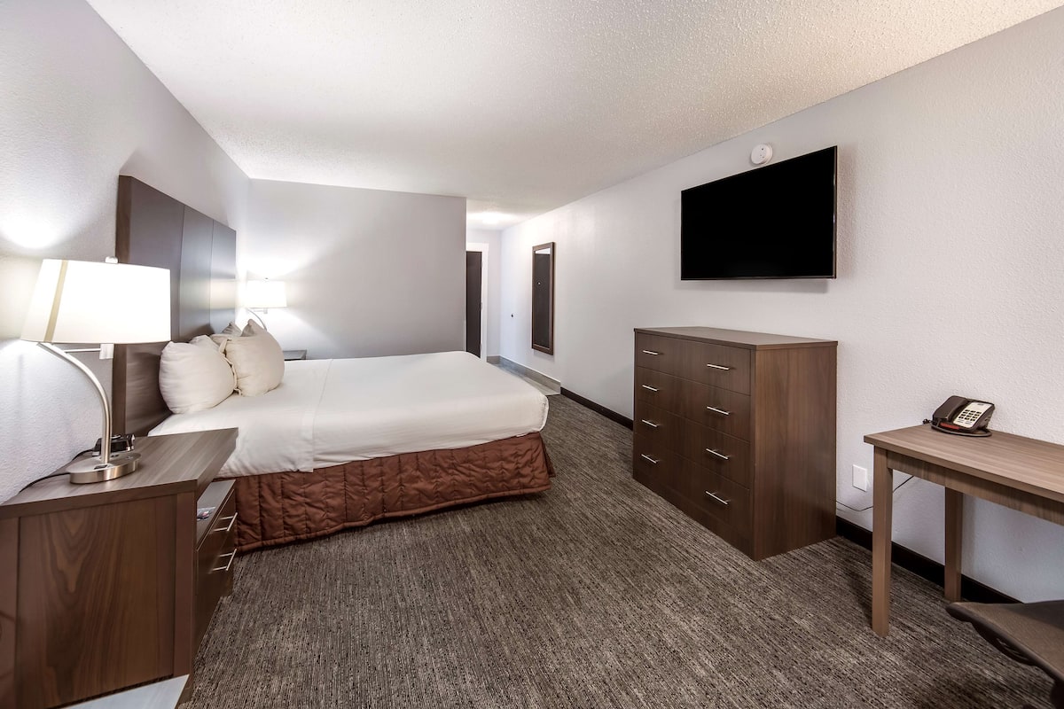 A hotel room with a bed, bedside table with a lamp, a desk with a telephone, a wardrobe, and a flat-screen TV mounted on the wall.